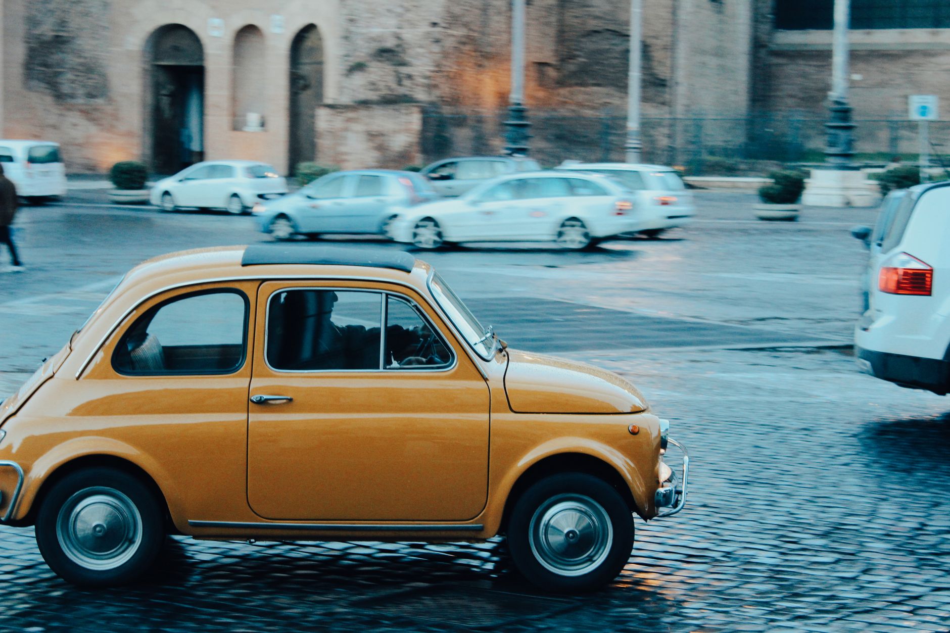 Żółty Fiat 500 jedzie po brukowanej ulicy w centrum Rzymu