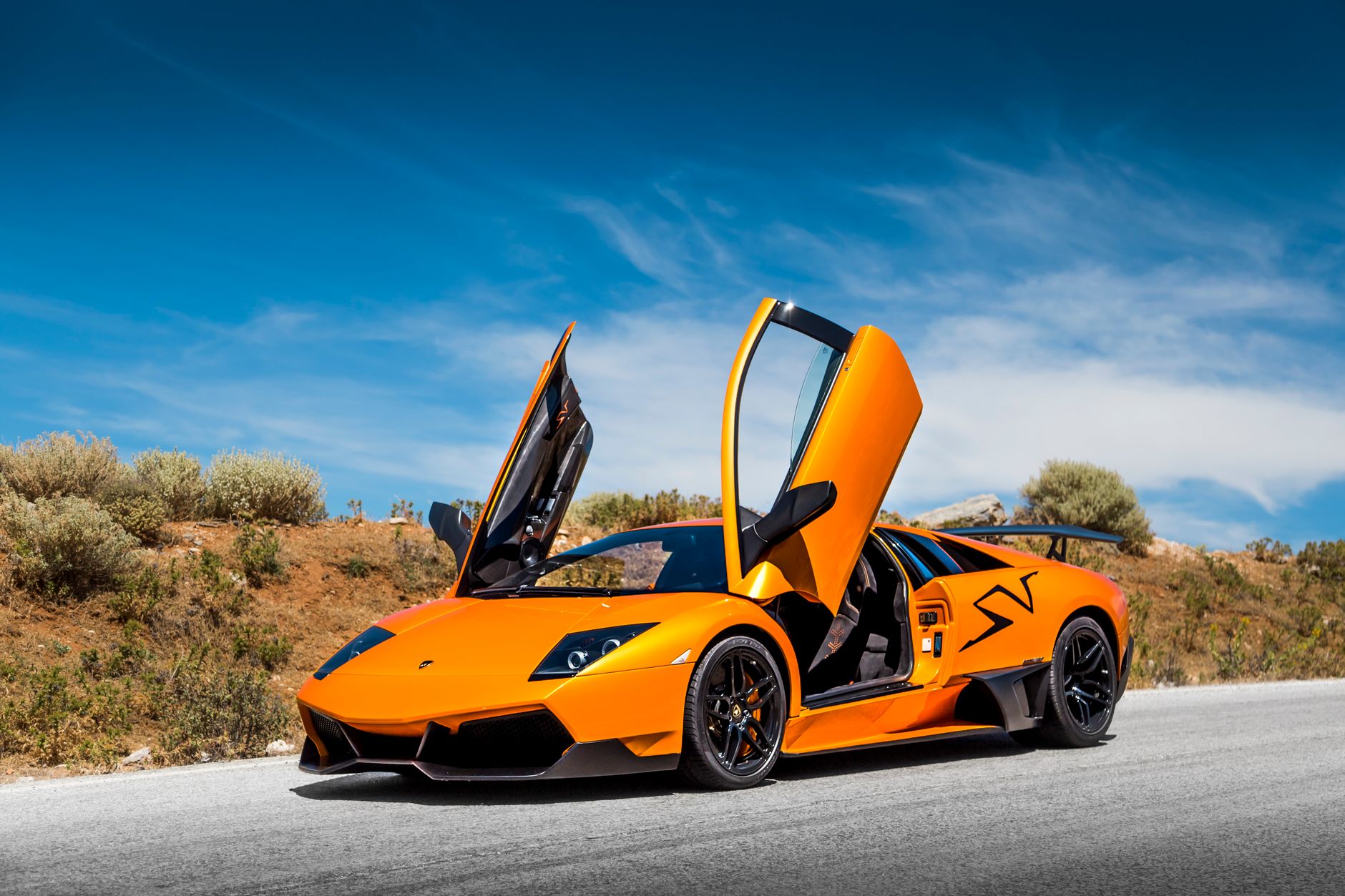 Pomarańczowe Lamborghini z otwartymi drzwiami na malowniczej drodze