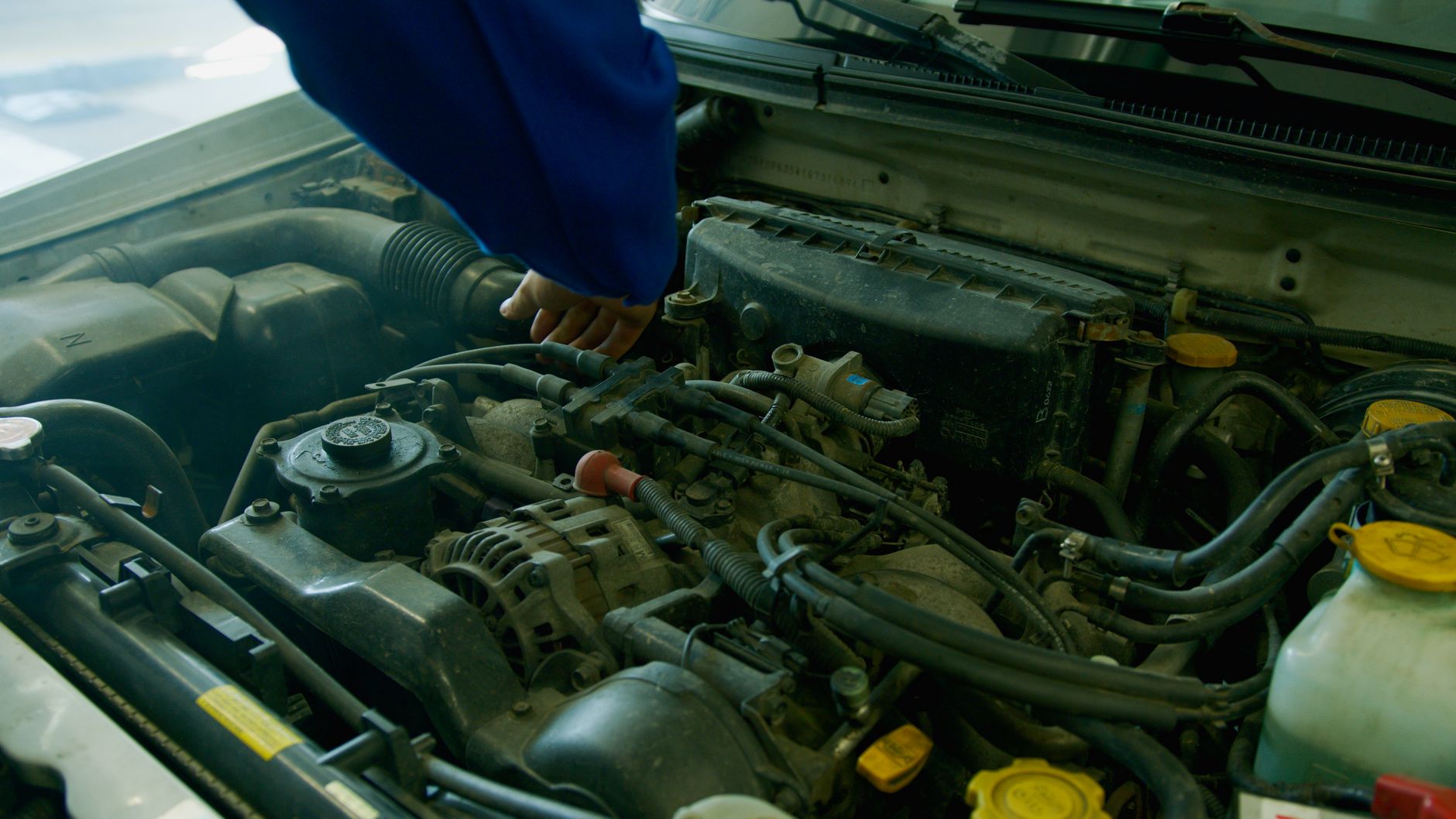 Mechanik w niebieskim kombinezonie naprawia silnik Volkswagena Passata B8