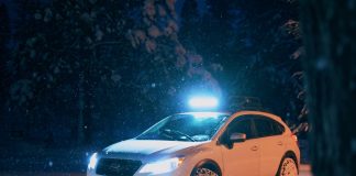 Biały samochód jedzie nocą zaśnieżoną drogą z włączonymi światłami