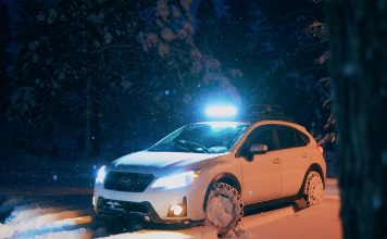 Biały samochód jedzie nocą zaśnieżoną drogą z włączonymi światłami